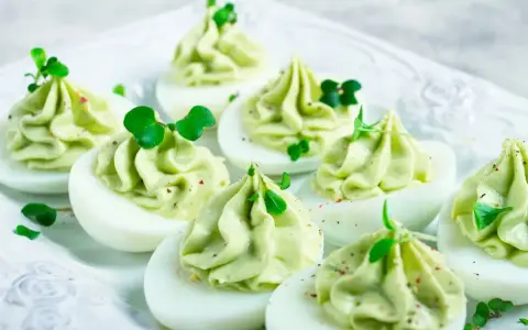 Uova ripiene per Pasqua, guarnite con crema verde e germogli freschi, un antipasto colorato e delizioso.