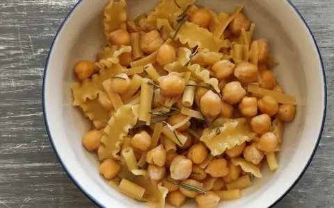 Un piatto invitante di pasta e ceci, con pasta corta e ceci dorati, guarnito con rosmarino fresco.