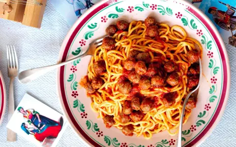 Un piatto di spaghetti alla chitarra con polpettine al sugo, serviti in un piatto decorato.