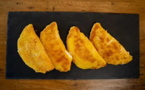Quattro sofficini fatti in casa, dorati e croccanti, serviti su una pietra nera.