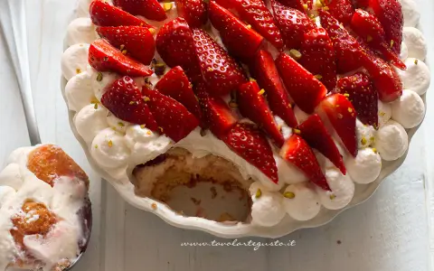 Delizioso tiramisù alle fragole, con panna montata, fragole fresche e pistacchi. Una fetta è già servita su un cucchiaio.