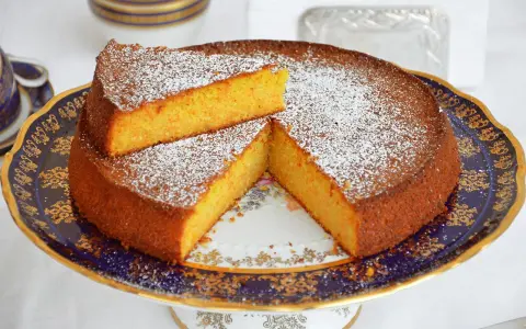 Deliziosa torta carote e mandorle, spolverata di zucchero a velo, servita su un elegante alzata.