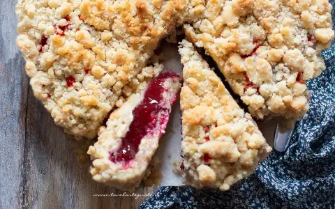Torta con marmellata, con crosta friabile e ripieno rosso brillante. Una fetta mostra la consistenza succosa.