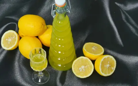 Limoncello fatto in casa: una bottiglia e un bicchierino di liquore giallo brillante, circondati da limoni freschi. La ricetta limoncello 1 litro alcool è pronta per essere gustata.