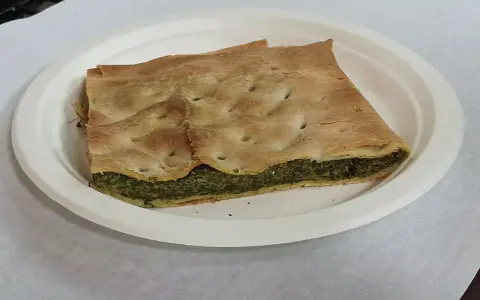 Una fetta di torta pasqualina originale genovese, con pasta sfoglia dorata e ripieno verde di spinaci e ricotta, servita su un piatto bianco.