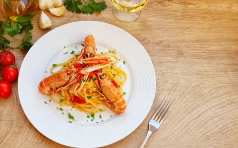Un piatto di linguine agli scampi, condite con pomodorini e prezzemolo, accompagnato da ingredienti freschi e un bicchiere di vino bianco.