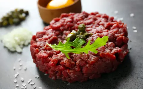 Battuta di fassona cruda, guarnita con capperi e rucola, con tuorlo d'uovo e cipolla tritata sullo sfondo.