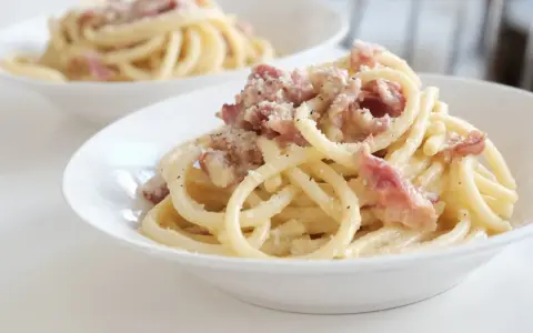 Un piatto di pasta alla gricia fumante, con guanciale croccante e pecorino romano grattugiato.