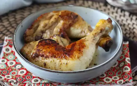 Cosce di pollo in padella, dorate e succulente, servite in una ciotola su un tovagliolo decorato.