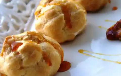 Bignè alla crema soffici e dorati, bagnati da un filo di caramello lucido su un piatto bianco.