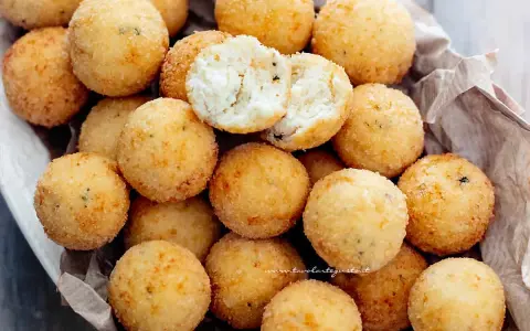 Un cesto pieno di croccanti polpette di ricotta, dorate e invitanti. Una è aperta, mostrando il morbido interno.