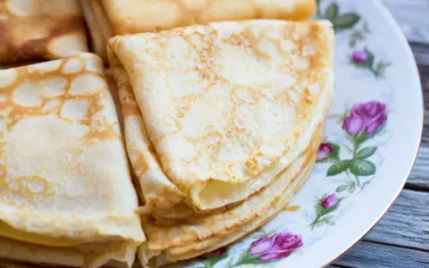 Deliziose crepes senza latte, piegate e impilate su un piatto decorato con rose. Perfette per una colazione leggera o uno spuntino.