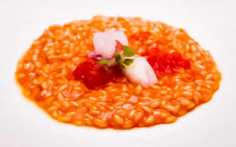 Un cremoso risotto al pomodoro, guarnito con calamari teneri, pomodorini e germogli freschi. Un piatto che celebra i sapori dell'Italia.