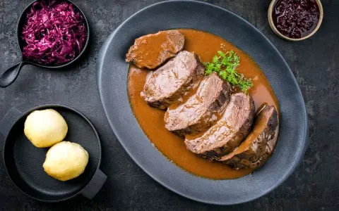Fette fette di girello di vitello in salsa, accompagnate da cavolo rosso e canederli.