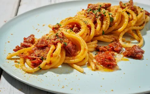 Spaghetti alla ghigliottina conditi con pomodorini secchi e pangrattato, un piatto invitante e saporito.