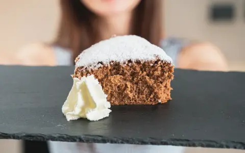 Una fetta di pan di spagna al cacao, soffice e spolverata di zucchero a velo, servita con panna montata su una lavagna scura.