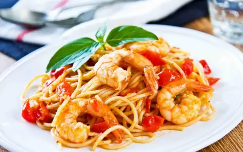 Un piatto invitante di spaghetti con gamberetti succulenti e pomodorini freschi, guarnito con basilico.