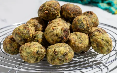 Pile di polpette ricotta e spinaci dorate e appetitose su una griglia metallica.