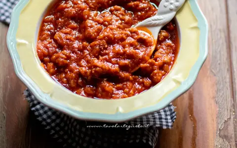 Un invitante sugo con salsiccia, denso e saporito, servito in una ciotola gialla con un cucchiaio decorato.