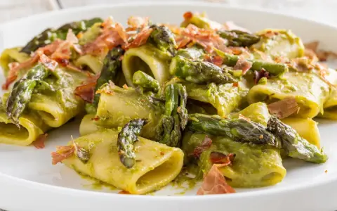 Paccheri conditi con una cremosa salsa verde e asparagi selvatici, guarniti con croccante prosciutto.