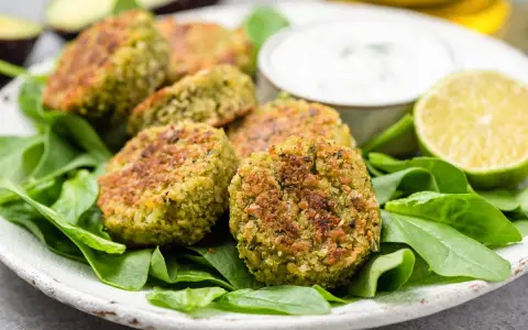Deliziose polpette di spinaci dorate, servite su un letto di spinacini freschi con salsa e spicchi di lime.