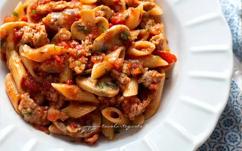 Piatto di pasta alla boscaiola con penne, funghi, salsiccia e pomodoro, condita con prezzemolo fresco.