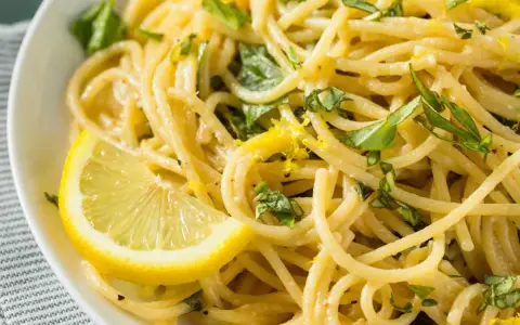 Un piatto invitante di spaghetti al limone, guarnito con scorza di limone e basilico fresco.