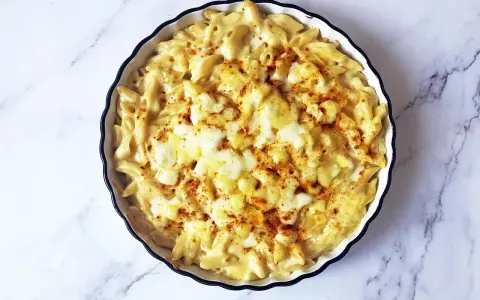 Piatto di mac and cheese fumante, con pasta penne cremosa e formaggio fuso, spolverato con paprika.