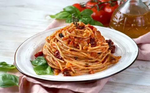 Un piatto di spaghetti conditi con un sugo rosso ricco di pomodori secchi, aglio e basilico fresco.