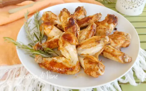 A plate of golden-brown, juicy chicken wings garnished with rosemary sprigs.