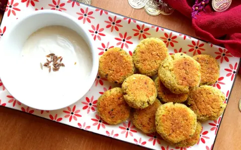 Falafel al forno dorati su un piatto decorato, accompagnati da una ciotola di salsa bianca con semi di cumino.