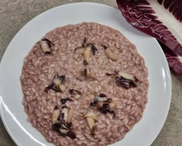 Un cremoso risotto al radicchio, con pezzetti di verdura che spuntano dal riso. Accanto, una foglia di radicchio fresco.