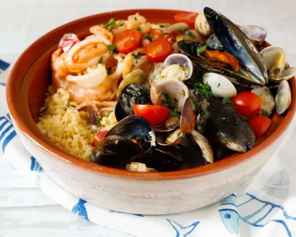 Un invitante cous cous di pesce, ricco di cozze, vongole, gamberi e pomodorini, guarnito con prezzemolo fresco.