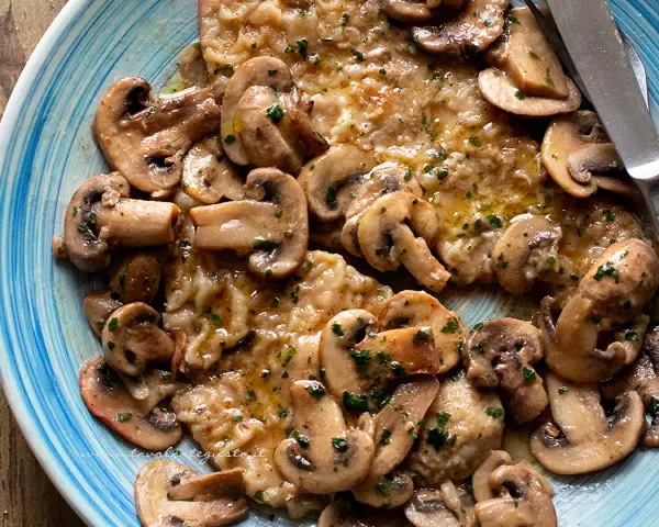 Scaloppine ai funghi, un piatto succulento con fettine di carne dorate e funghi champignon trifolati, guarnito con prezzemolo fresco.