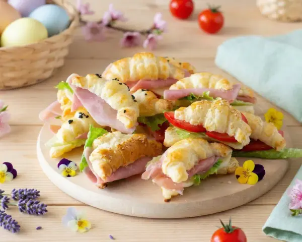 Delizioso antipasto di Pasqua con croissant farciti, uova colorate in un cesto e fiori primaverili.