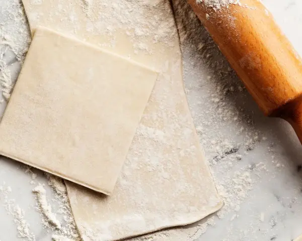 Farinata e mattarello su piano di marmo, pronti per creare pasta sfoglia fatta in casa.