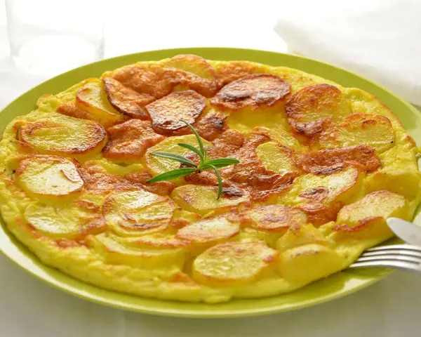Frittata di patate dorata e gustosa, guarnita con rosmarino fresco, servita su un piatto verde.