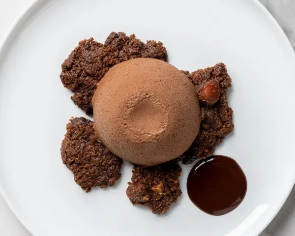 Semifreddo al cioccolato su croccanti biscotti al cacao, con una nocciola intera e una goccia di salsa al cioccolato.