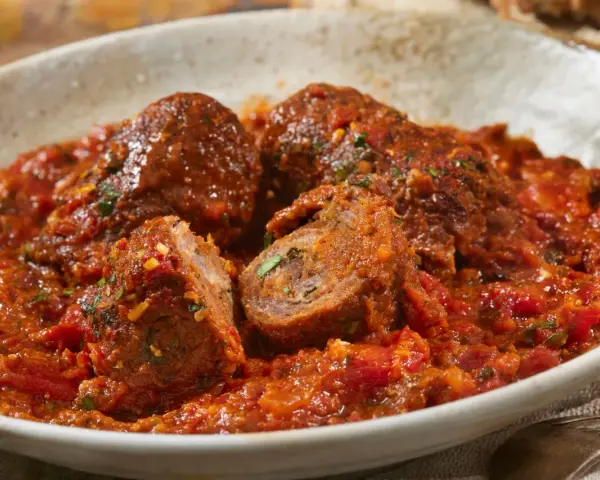 Involtini alla romana succulenti in un ricco sugo di pomodoro, con un interno visibile che rivela erbe aromatiche.