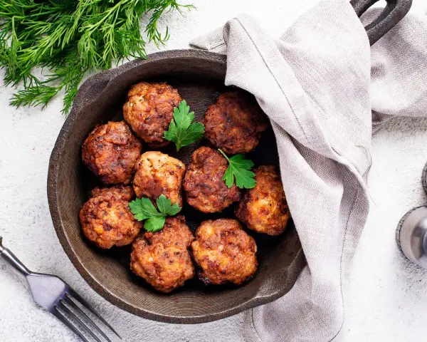 Polpette senza uova dorate in padella, guarnite con prezzemolo fresco. Un piatto gustoso e leggero, pronto per essere gustato.