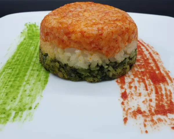 Un colorato timballo di riso a tre strati, con salse verdi e rosse che ricordano i colori di una bandiera.