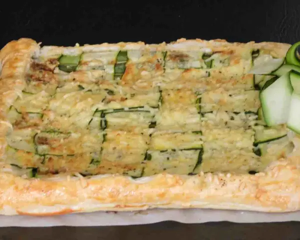 Torta salata con pasta sfoglia e zucchine a griglia, ricoperta di formaggio fuso e guarnita con fettine di zucchina fresca.