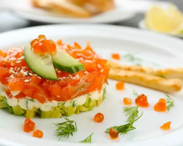 Tartare di salmone e avocado, un'idea per antipasti velocissimi senza cottura, guarnita con uova di pesce e cetriolo.