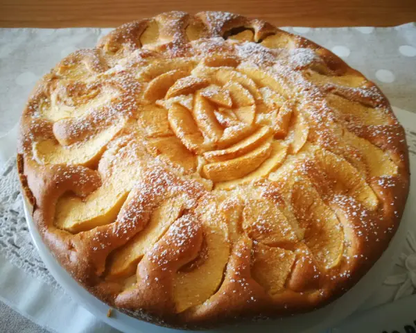 Deliziosa torta di mele senza glutine, decorata con mele a forma di rosa e spolverata di zucchero a velo.