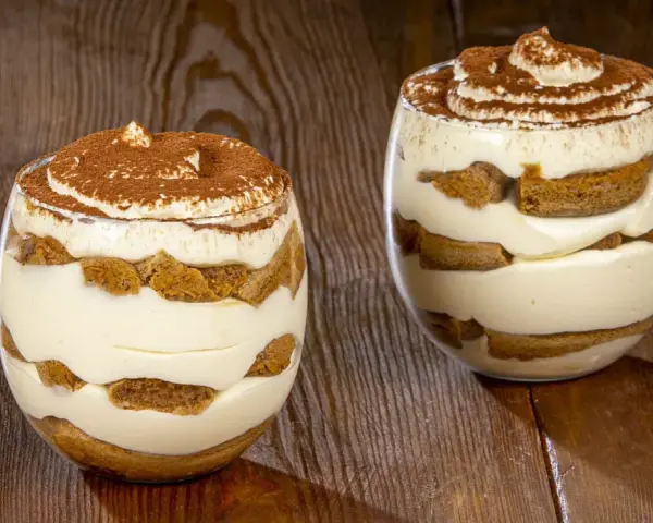 Due bicchieri di delizioso tiramisù senza uova, con strati di savoiardi e crema, spolverati di cacao.