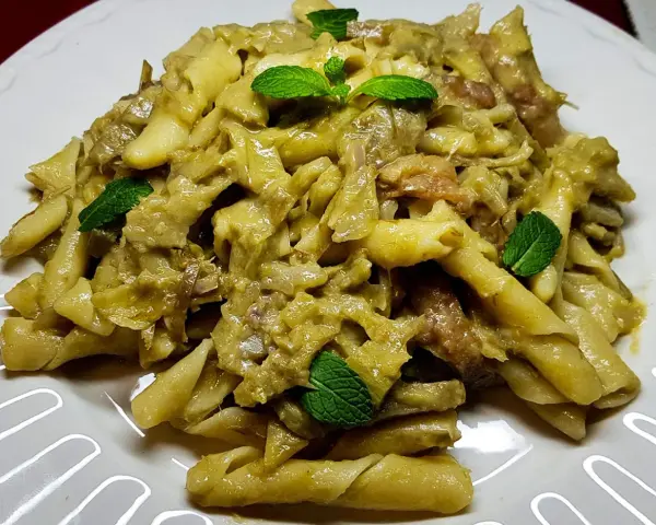 Pasta con carciofi cremosa, guarnita con foglie di menta fresca. Un piatto saporito e invitante.