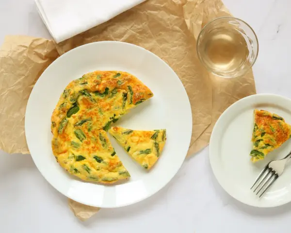 Deliziosa frittata di asparagi al forno, servita su un piatto bianco con una fetta a parte e un bicchiere di vino.