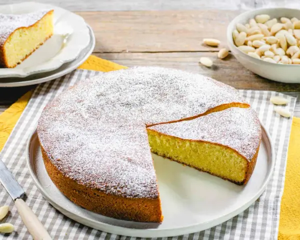 Torta soffice con farina di mandorle, spolverata di zucchero a velo. Un pezzo è già stato tagliato, pronto per essere gustato.