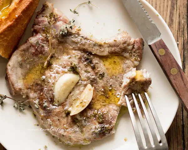 Succulente braciole di maiale cotte con aglio e erbe aromatiche, servite con pane croccante.