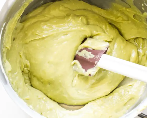 Una spatola mescola una densa crema al pistacchio in una ciotola d'acciaio.